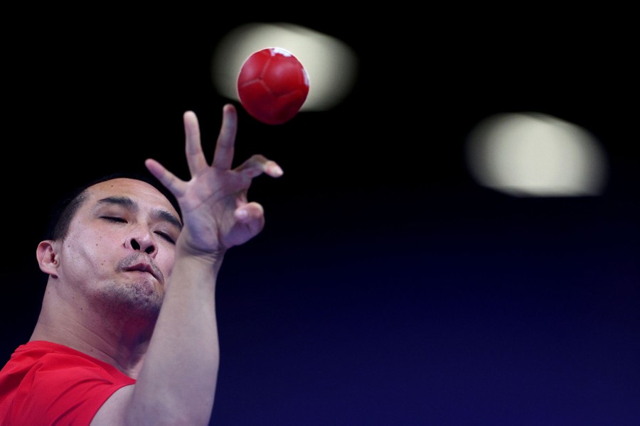 A para-athlete throws a small red ball during a boccia match.