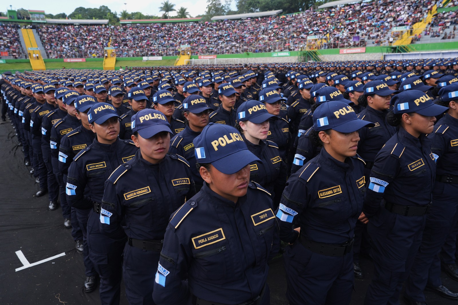 A large group of new police officers stand in even rows in a stadium during a graduation ceremony.