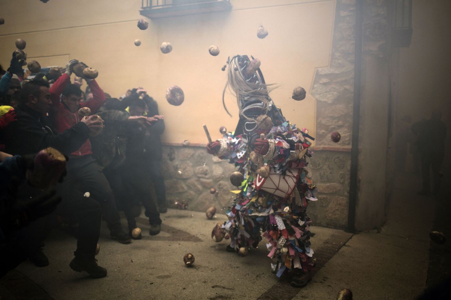A costumed figure is pummeled by turnips thrown by a group of people.
