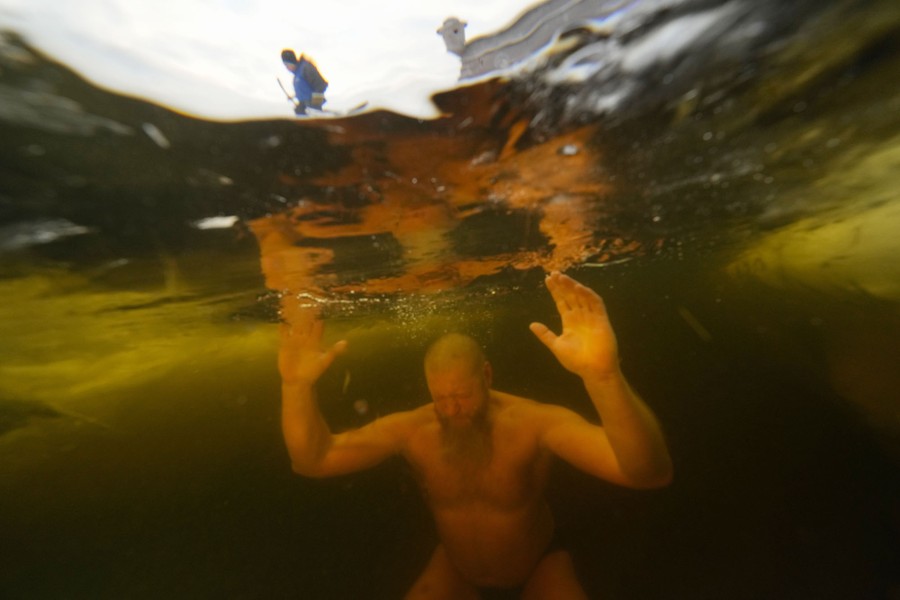 A man is seen underwater, and a person wearing a winter coat is visible above the surface.