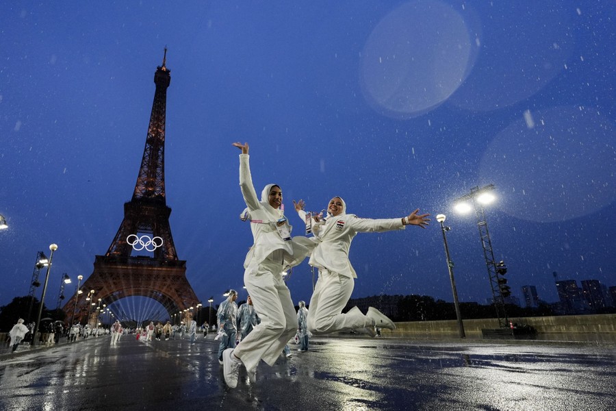 Two athletes jump in the air in front of the Eiffel Tower on a rainy night.