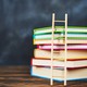 stack of multicolored notebooks with a small wooden ladder leaning propped up against the stack
