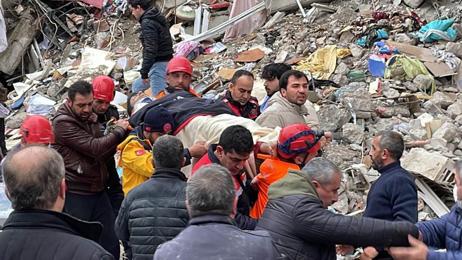 People carry a person on a stretcher away from the rubble of a collapsed building.