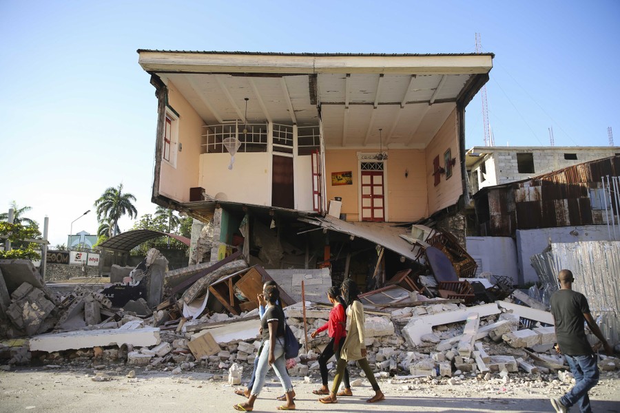 People walk past a home destroyed by the earthquake in Les Cayes.