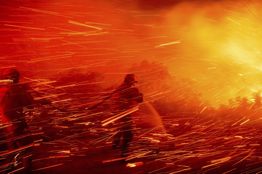 Two firefighters use a hose to spray water amid a swirl of wind-blown embers.