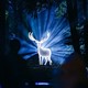 A life-size cutout sculpture of a stag glows, surrounded by backlighting, displayed in a forest setting.