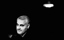 A black-and-white photo of Qassem Soleimani, looking downward to the left of the camera