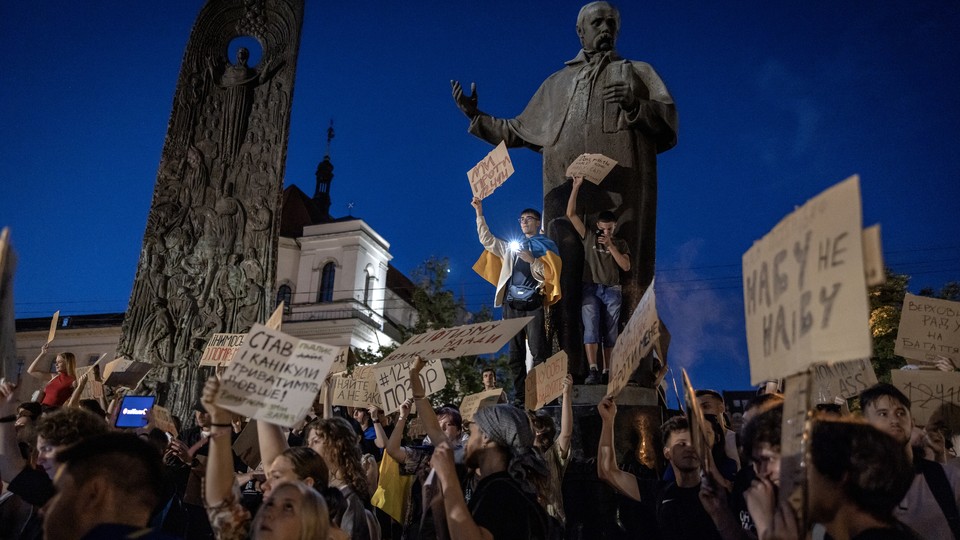 Photograph of Ukrainians protesting near the monument of a poet, holding up homemade cardboard signs