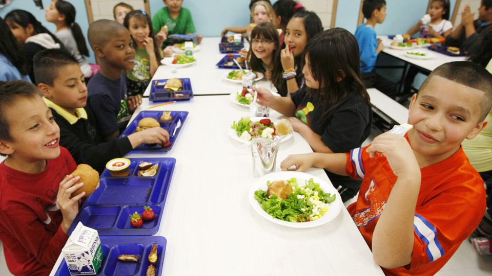 Young students at a cafeteria table eat lunch