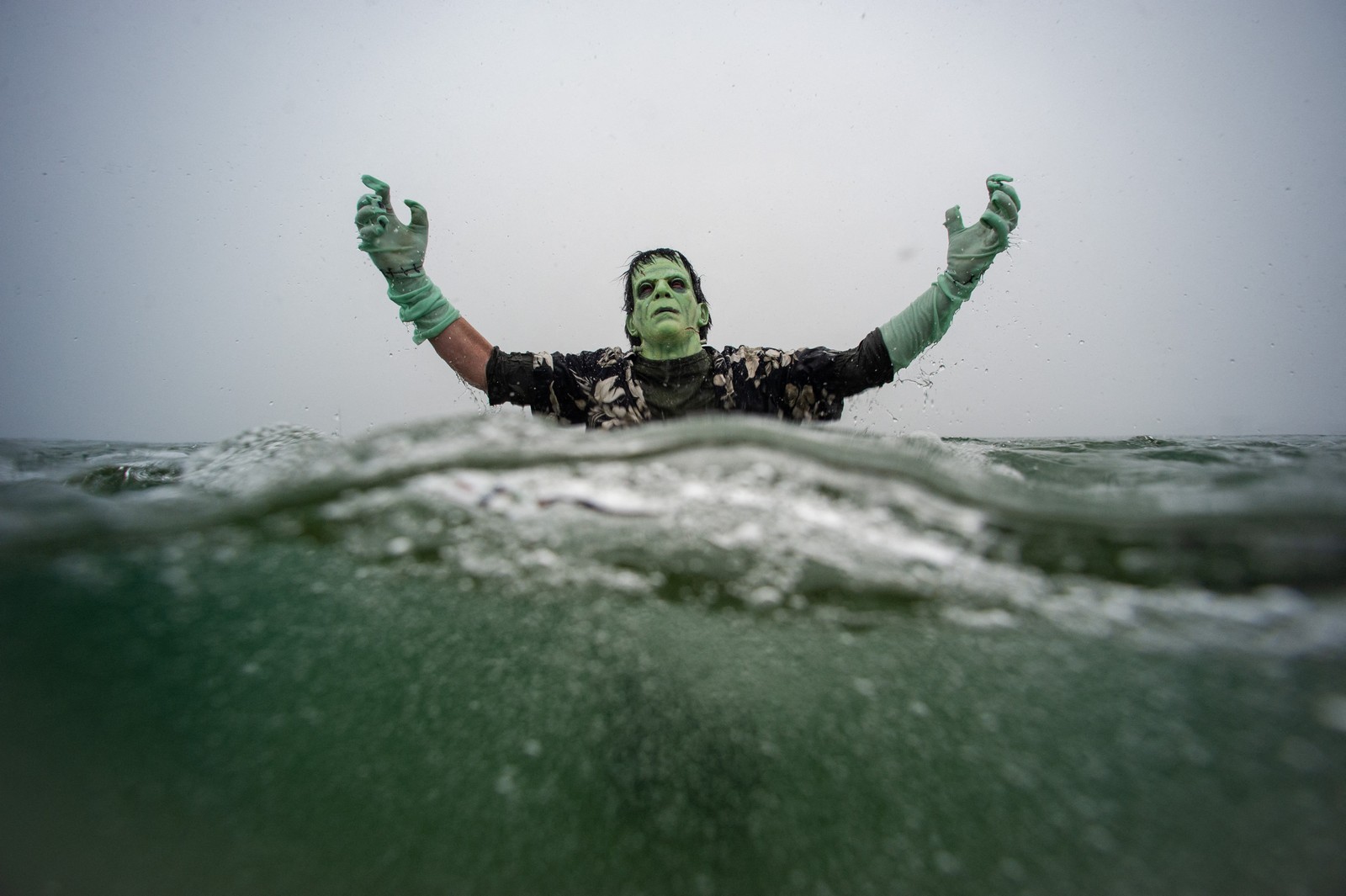 A reveler dressed as Frankenstein's monster plunges into the ocean during a polar bear plunge event.