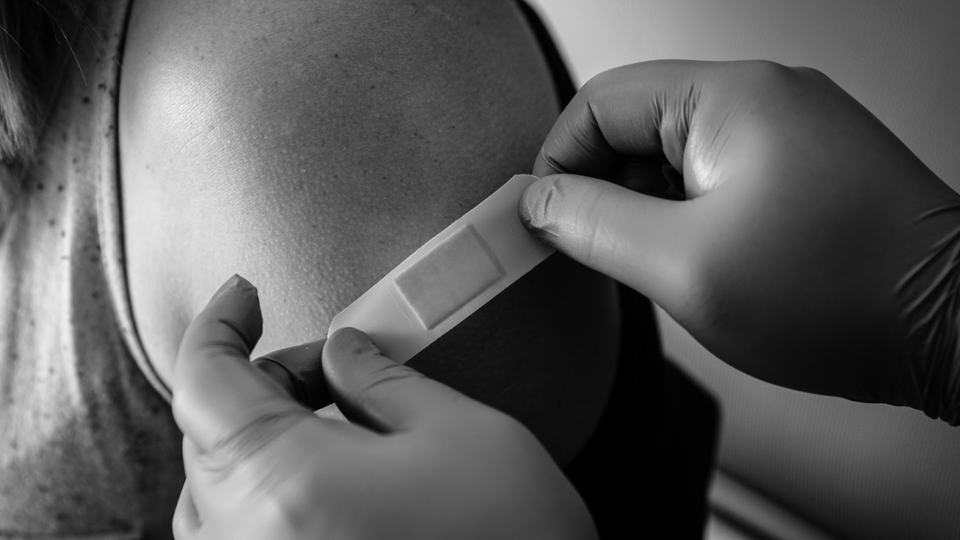 Black and white image of someone getting a band-aid after a shot