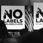 A conference room full of people, American flags, and signs that say "No Labels"