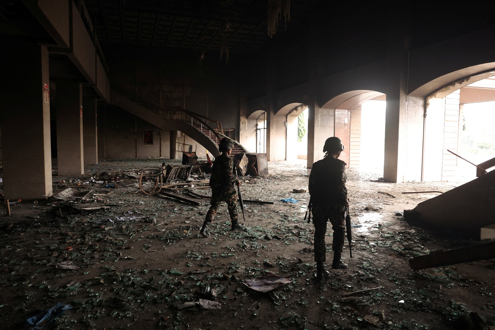 Two soldiers walk through debris inside the scorched entryway of a government building.
