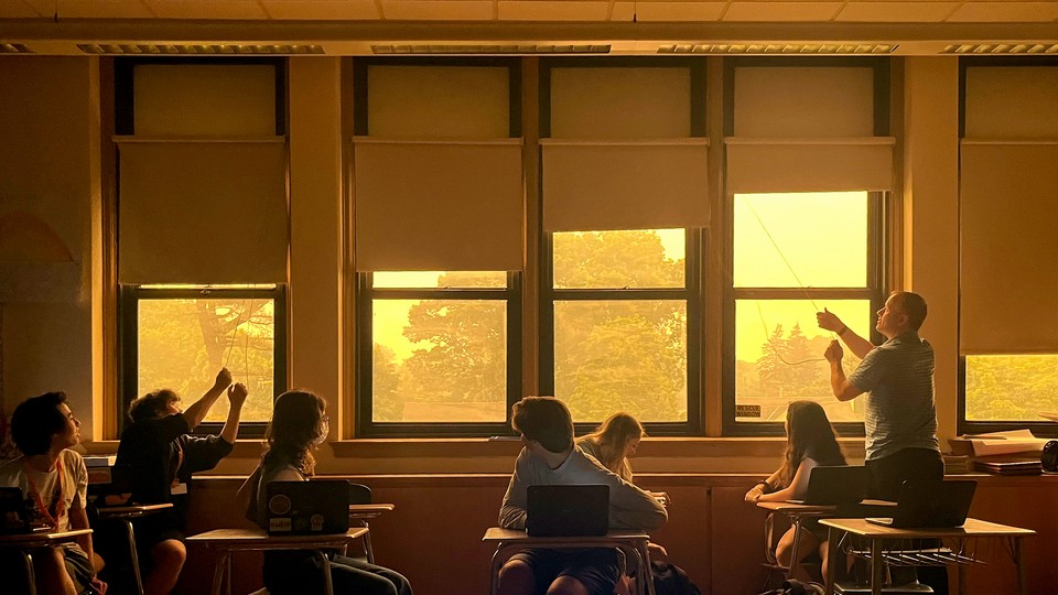 A teacher closes the shades of windows looking out on a haze of wildfire smoke.