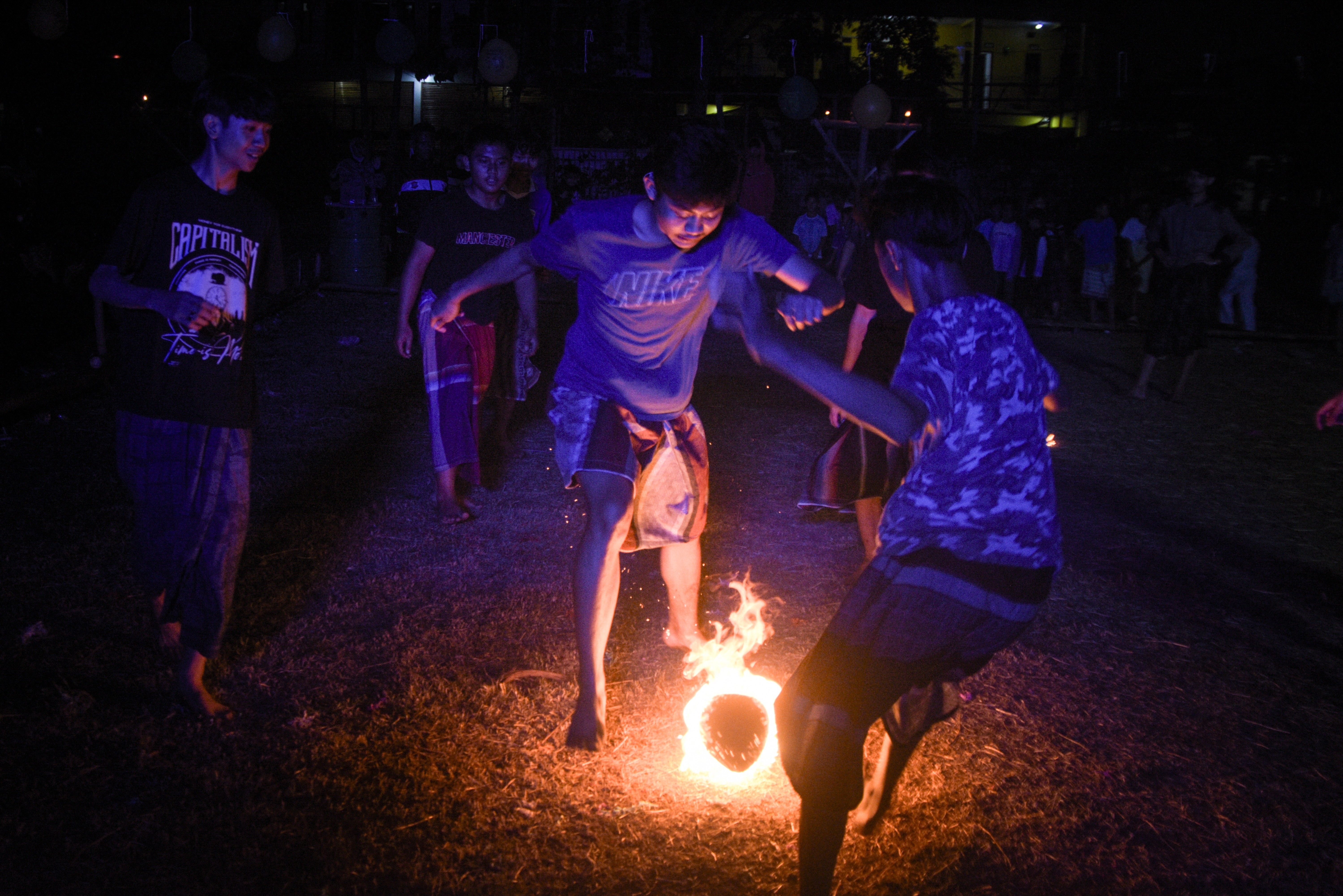 Young people play a game, kicking a flaming coconut.