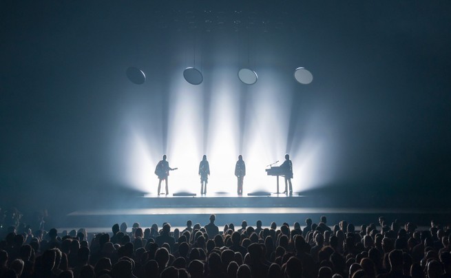 photo of a stage with four backlit silhouettes in front of an audience