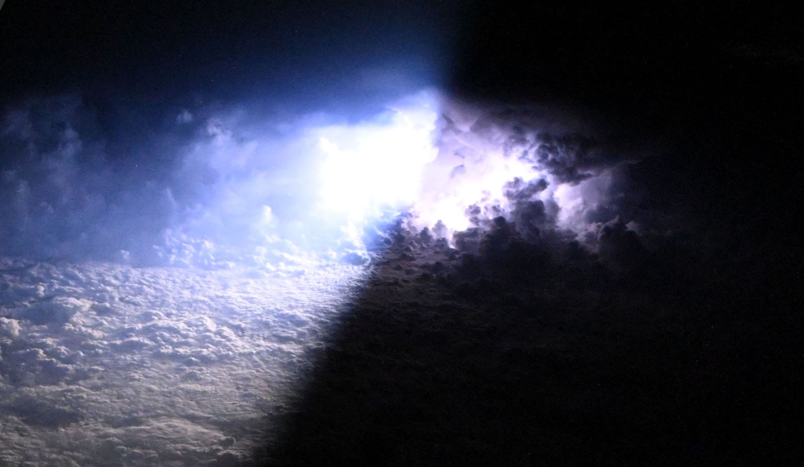 A bolt of lightning casts shadows and illuminates storm clouds from within.