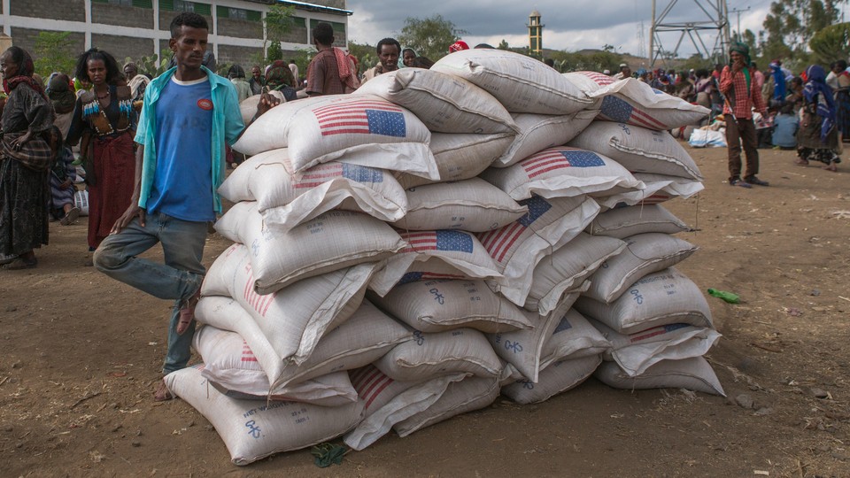 A man standing on a dirt road next to several large bags of food with the American flag on them