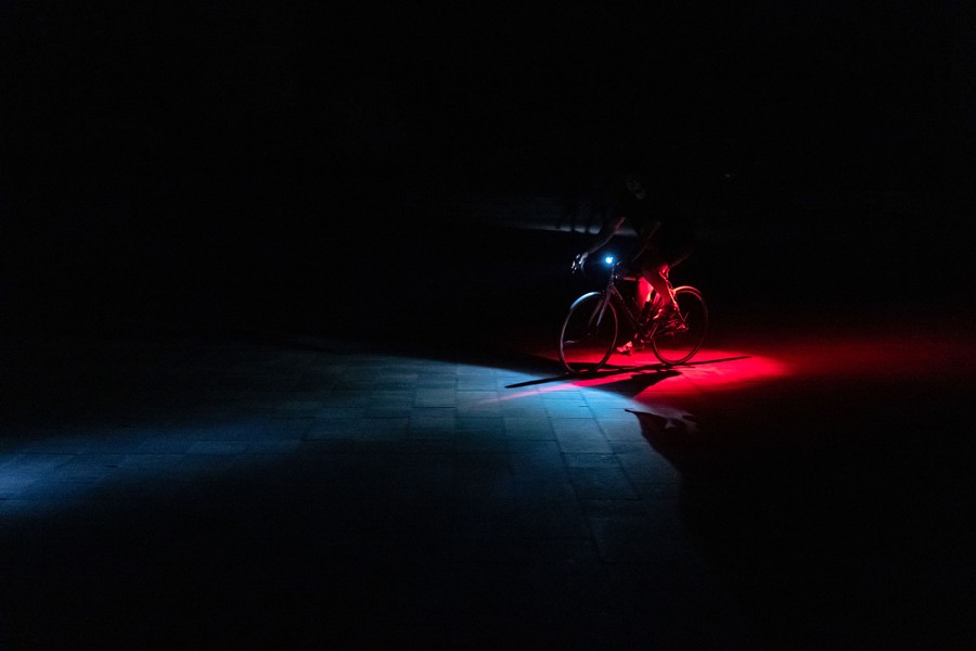 Patches of white and red light shine from lamps on a bicycle as it passes by on a dark street.