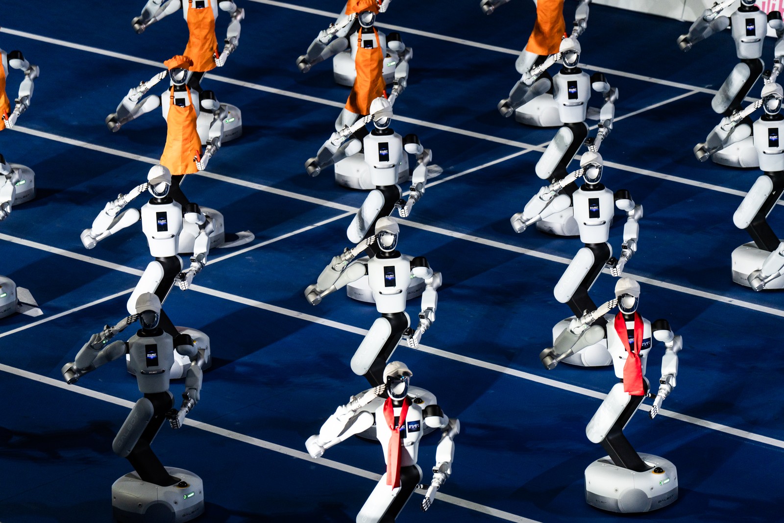 A group of robots move along an indoor track, saluting.