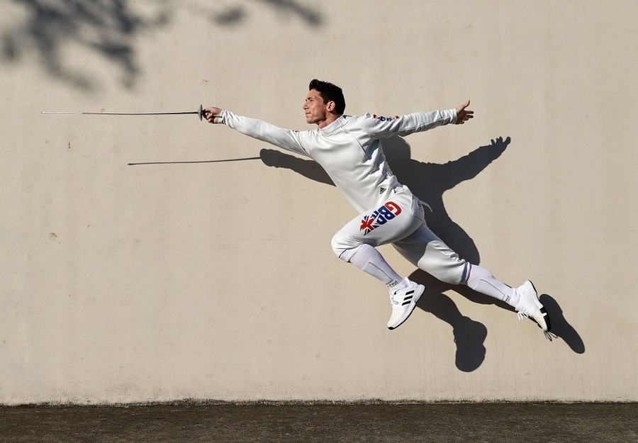 A fencer leaps with his sword, posing for a portrait.