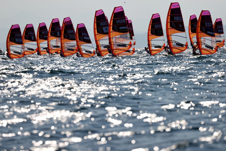 More than a dozen windsurfers sail across a harbor together.