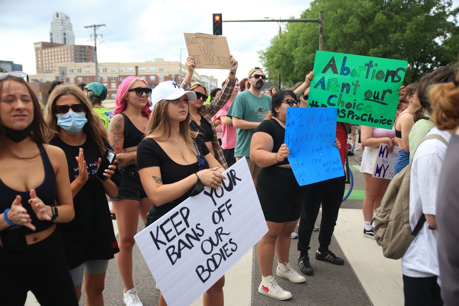 Protesters stand in a street holding signs, including one that reads "Keep your bans off our bodies."
