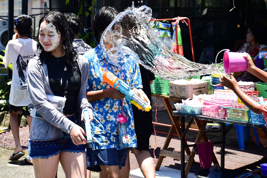 A person throws a small bucket of water at two people walking by.