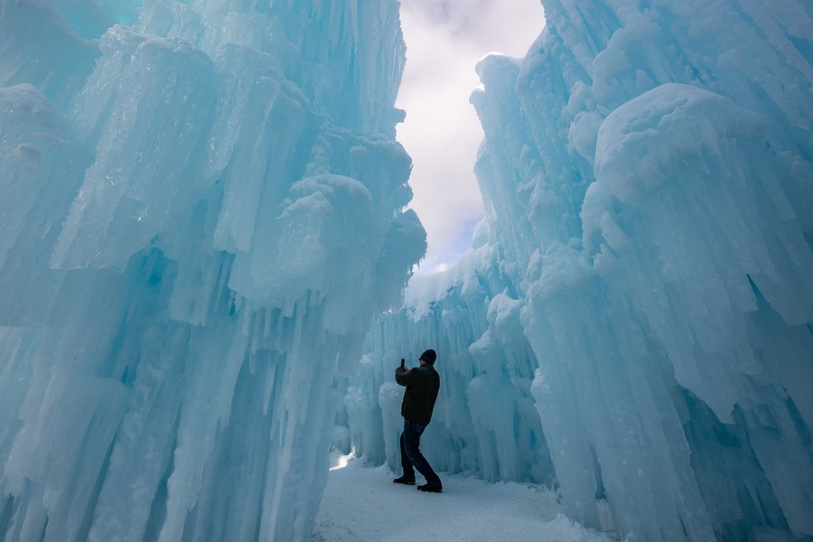 A person takes pictures while standing inside a narrow passage between blue-white ice walls.