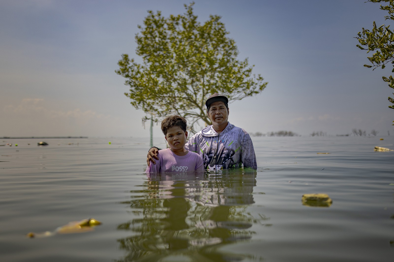 A man and a boy stand side-by-side in chest-deep floodwater.
