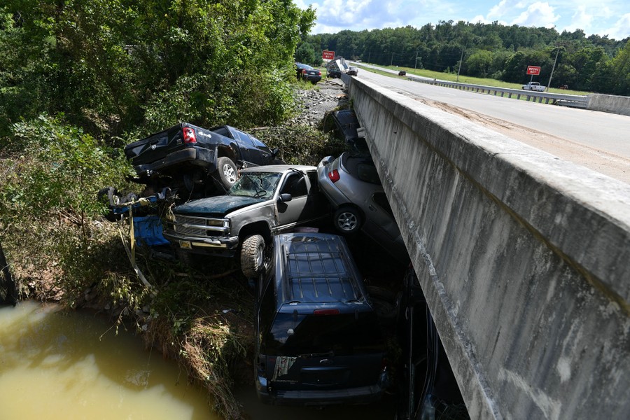Cars and trucks sit piled against a bridge.
