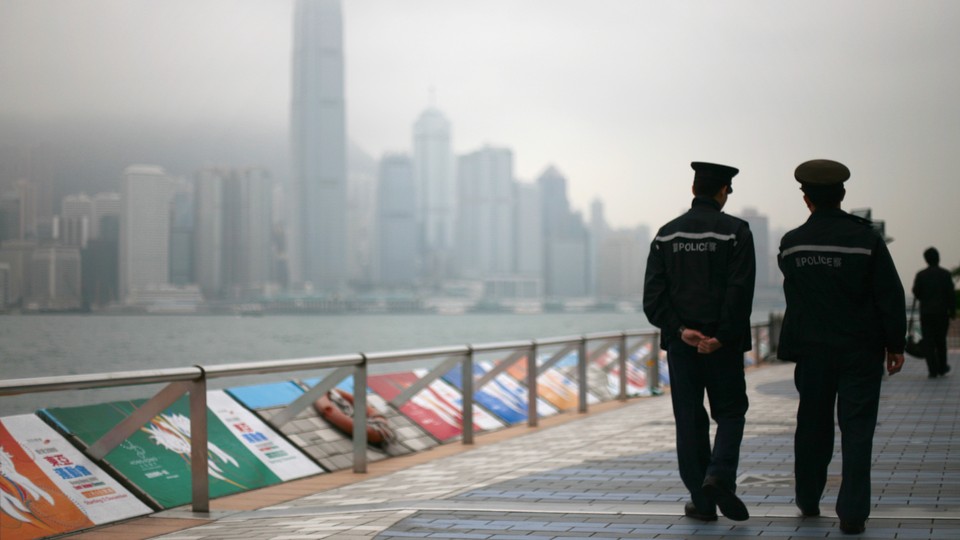 Two people walk down a path next to a waterfront with tall buildings in the background.