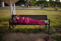 A woman wearing a face mask sleeps on a bench in Seoul.