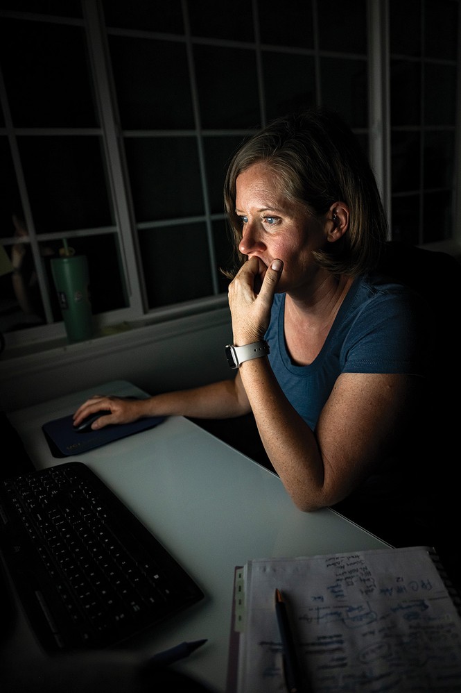 photo of woman at night, sitting at desk lit by computer monitor, with one hand to her face