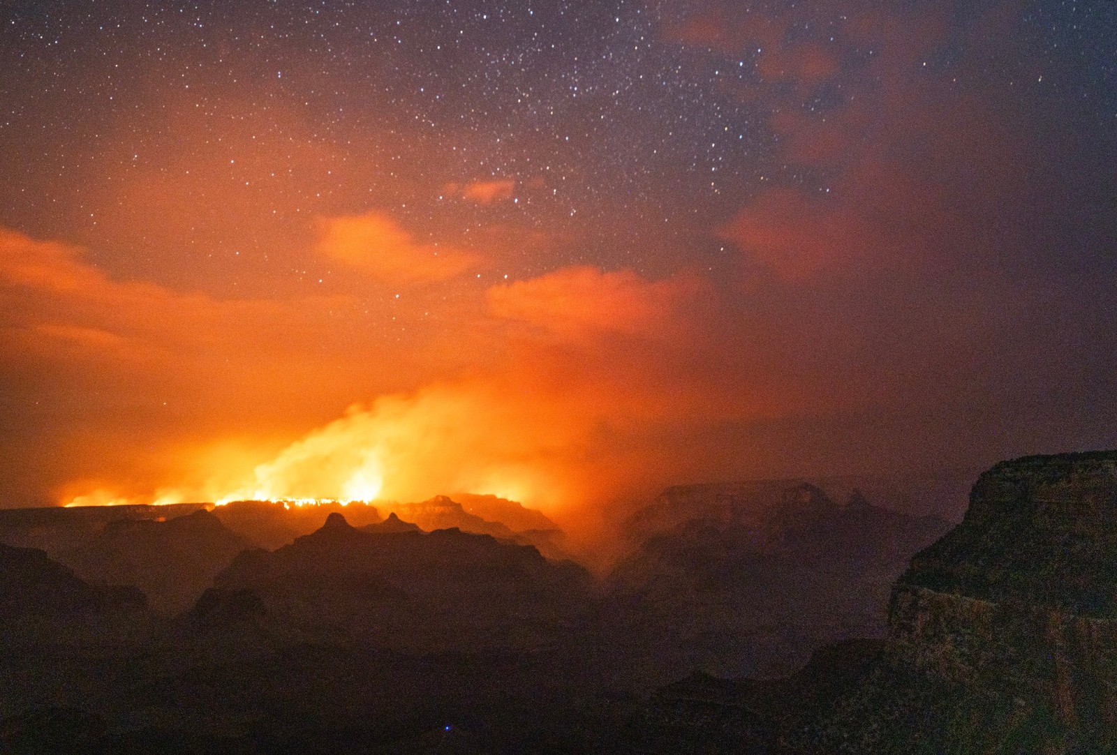 A broad view of a wildfire burning in the distance at the Grand Canyon, seen at night.