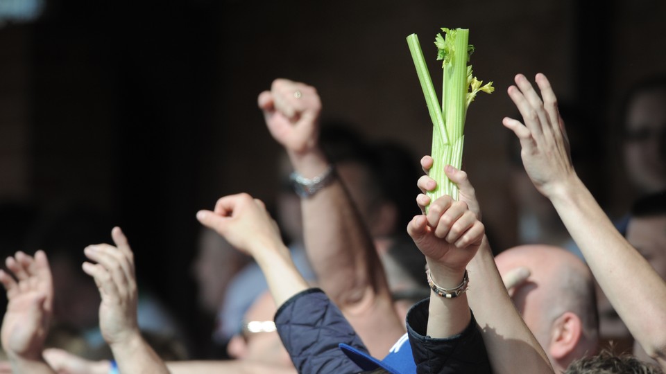 A man in a crowd holds a stalk of celery aloft.