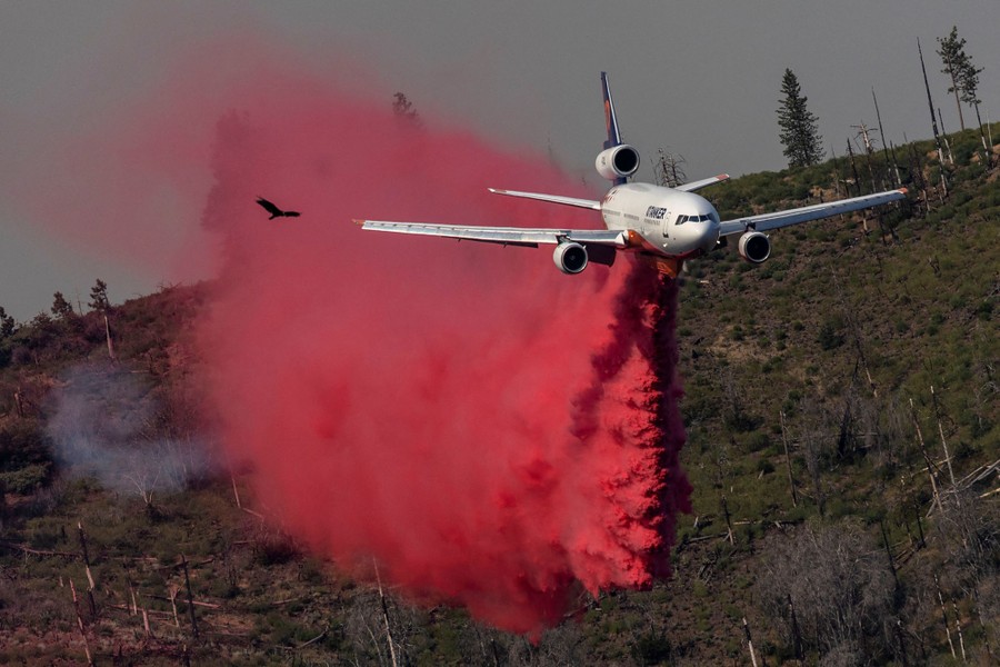 A large firefighting aircraft drops flame retardant on a hillside.