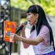 The drag queen Yuhua Hamasaki holds up "The Family Book" on an outdoor stage holding a microphone.
