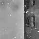 Black-and-white image of snow falling between buildings