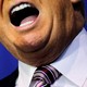 The lower half of Donald Trump's face and neck, showing his mouth open behind a microphone