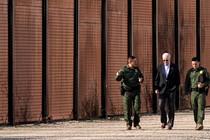 Biden walking with two police officers, the border wall in the background.