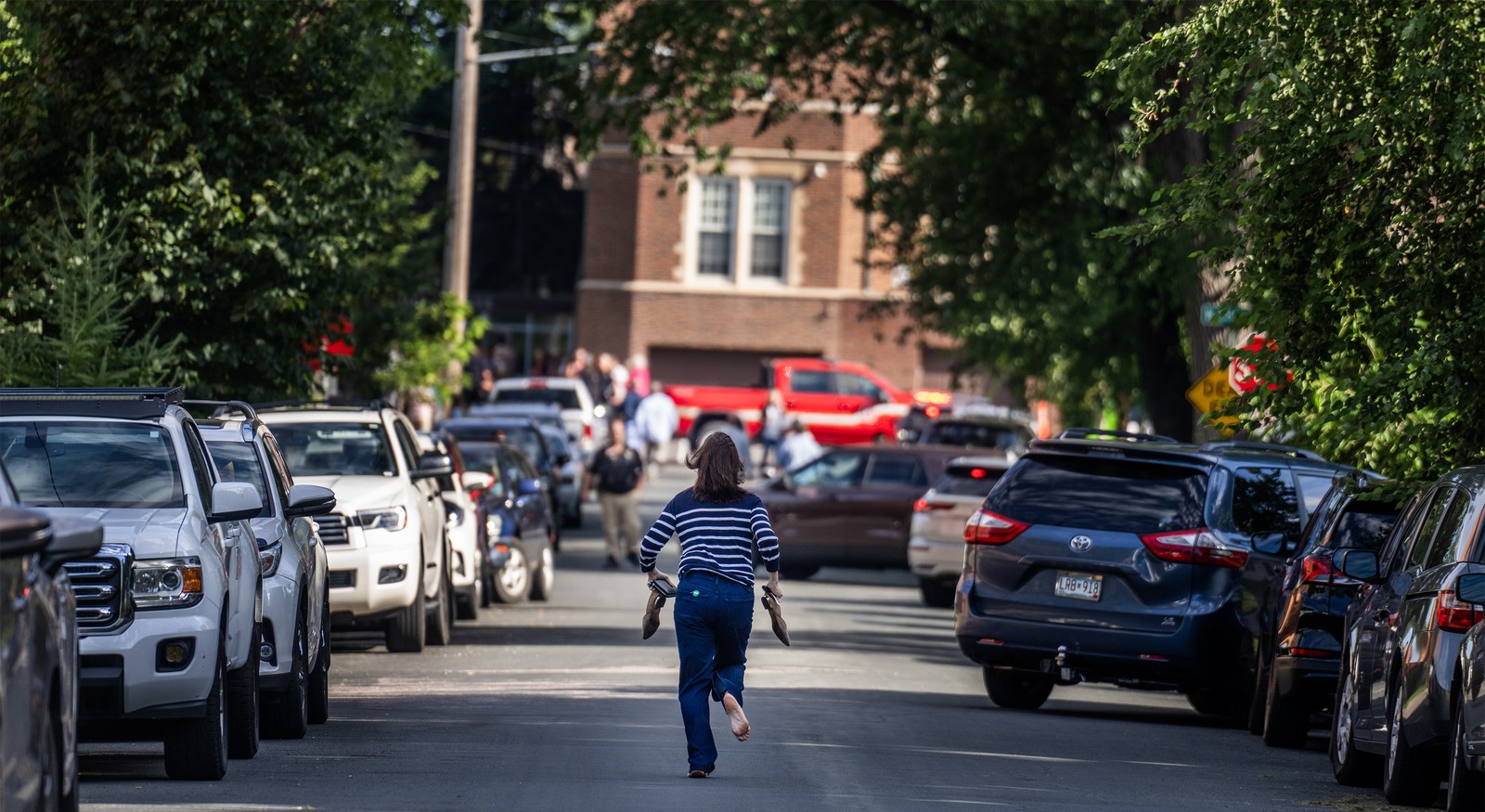 A parent runs down a street toward a school, barefoot, hurrying toward the scene of a shooting.