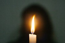 A photograph showing a candle in front of a silhouette of a person