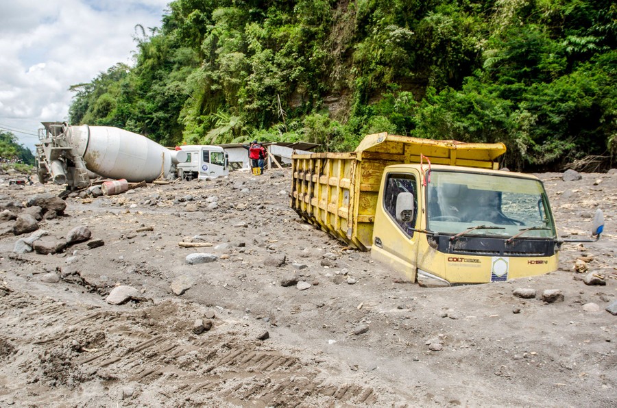 Several large trucks sit half-buried in ash and rocks.