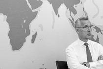 Jens Stoltenberg sits with his arms folded in front of a map of the world.