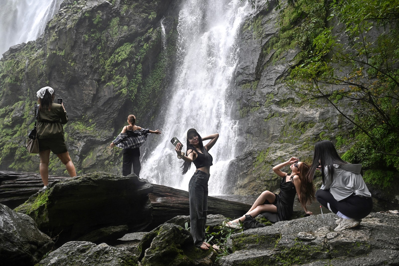 Several people take selfies or portraits of each other in front of a waterfall.