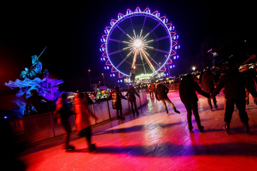 People ice skate in a rink near a Ferris wheel.