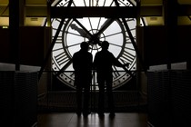 Two people are backlit while looking at a large clock