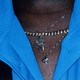 A close-up of an upper chest with a bright-blue shirt and three necklaces, including a gold chain and half a heart