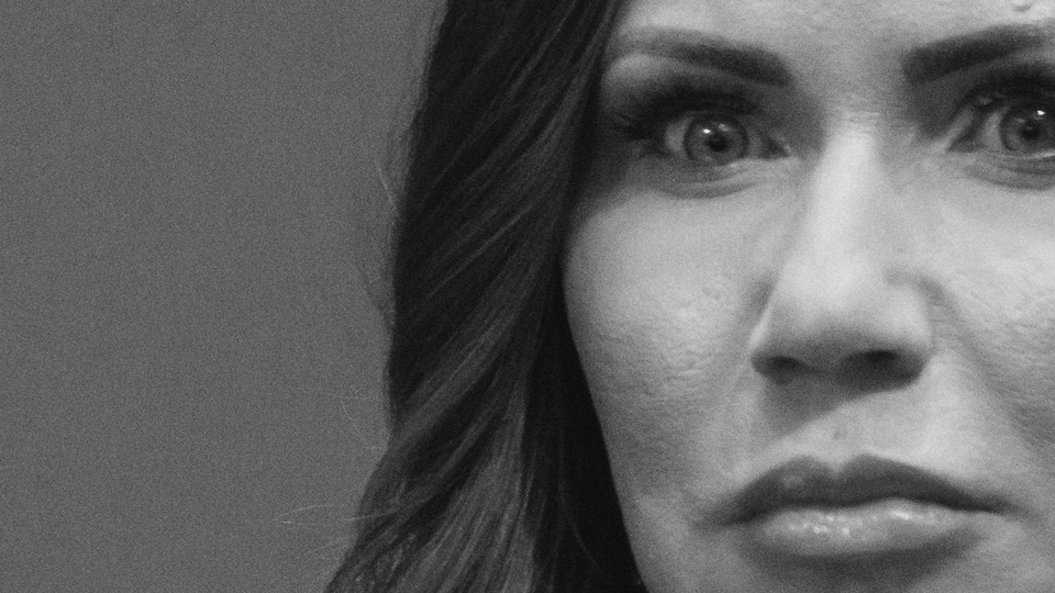 A close-up black-and-white photo of Kristi Noem's face